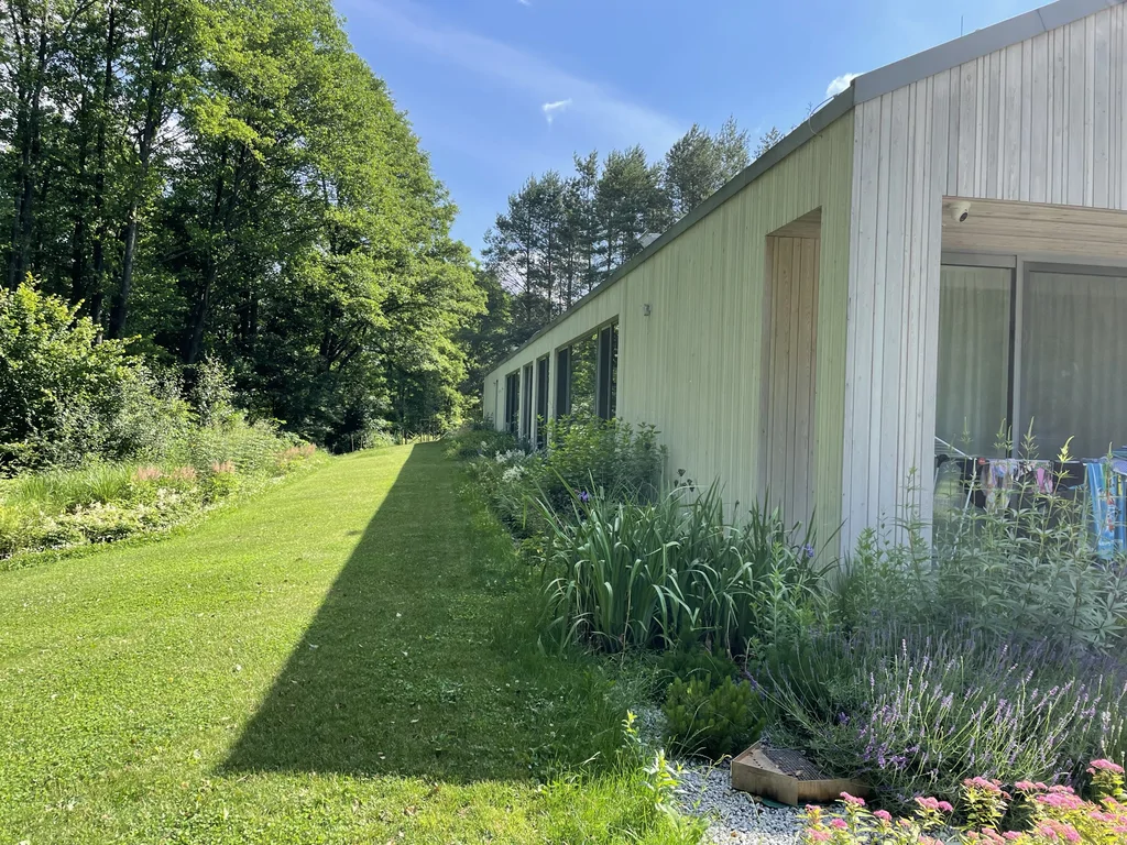 Widok boczny wzdłuż elewacji – pas zieleni i nasadzenia przy budynku, stolarka wielkoformatowa