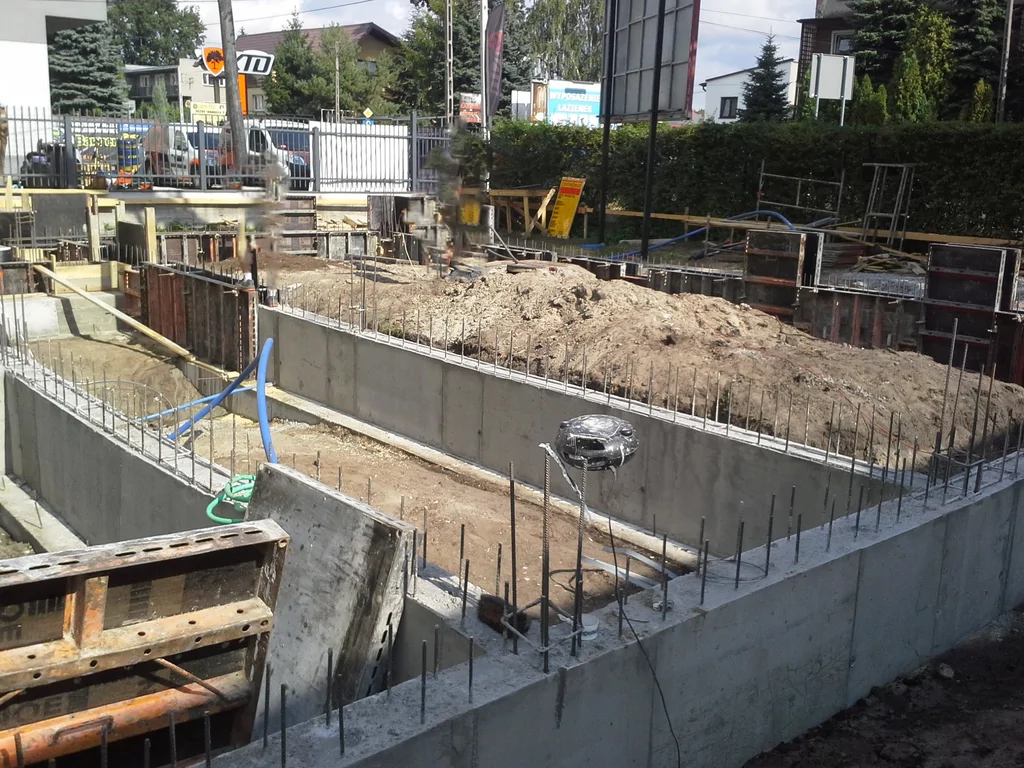 Wylane ściany fundamentowe żelbetowe posadowione na ławach wylanych na studniach. W tle szalunki. 
