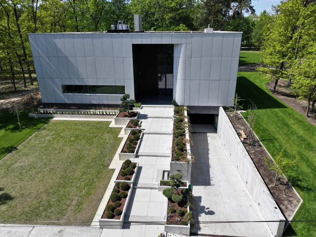 Front domu widziany z góry z wyeksponowanym dojściem do wejścia, donicami oraz zjazdem do garażu podziemnego