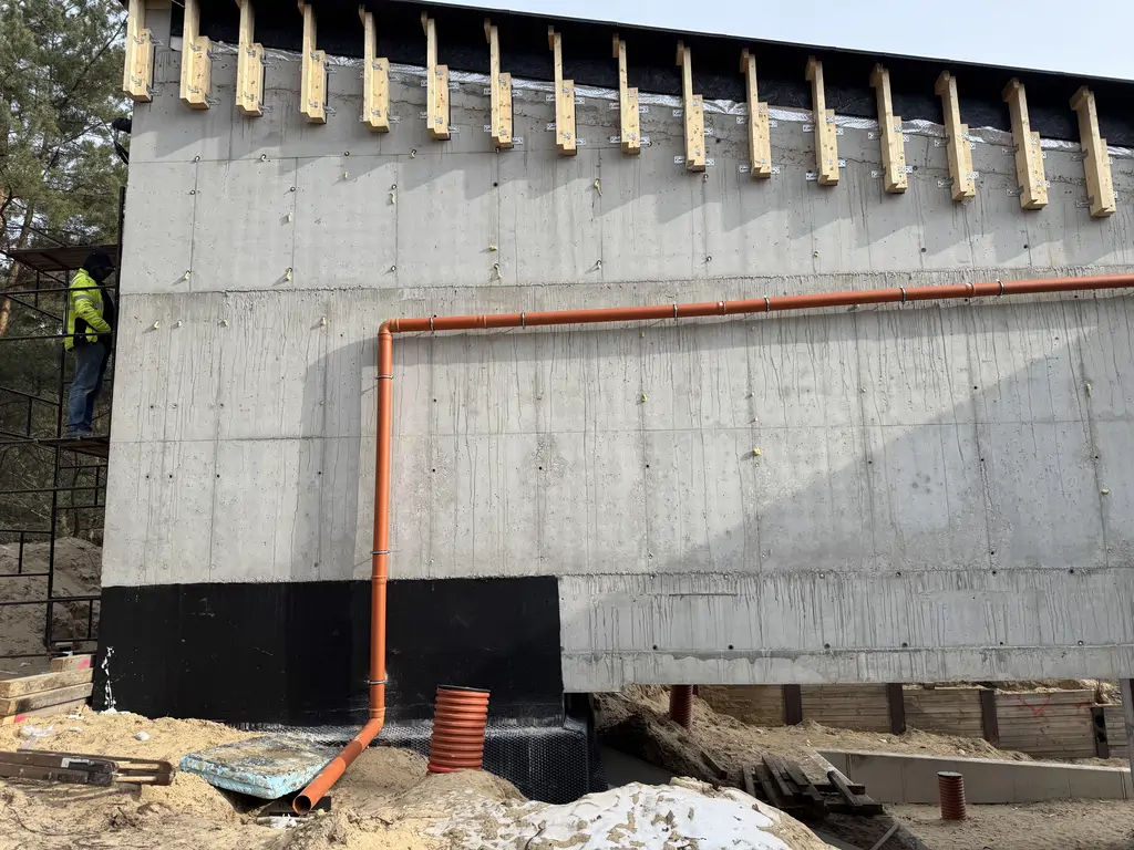 Żelbetowa ściana patio z oknem na piętrze i dużymi przeszkleniami na parterze.