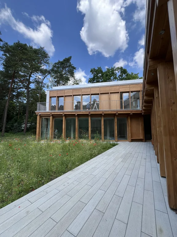 Widok z dziedzińca na nowoczesny budynek z drewnianą elewacją, tarasem i dużymi oknami