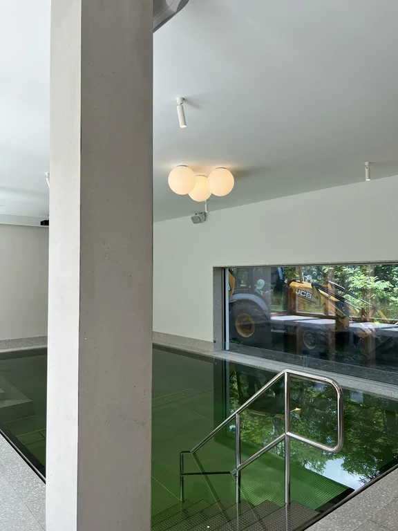 Wewnętrzny basen z betonowym słupem, schodami wejściowymi i dużym oknem na ogród