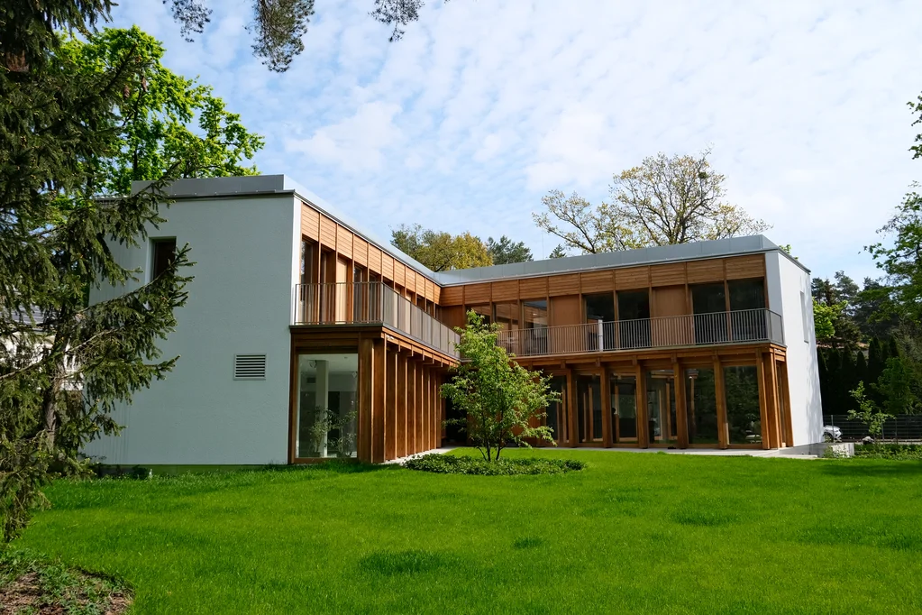 Szerokie ujęcie ogrodowe domu z narożną bryłą, drewnianą elewacją i rozległym trawnikiem