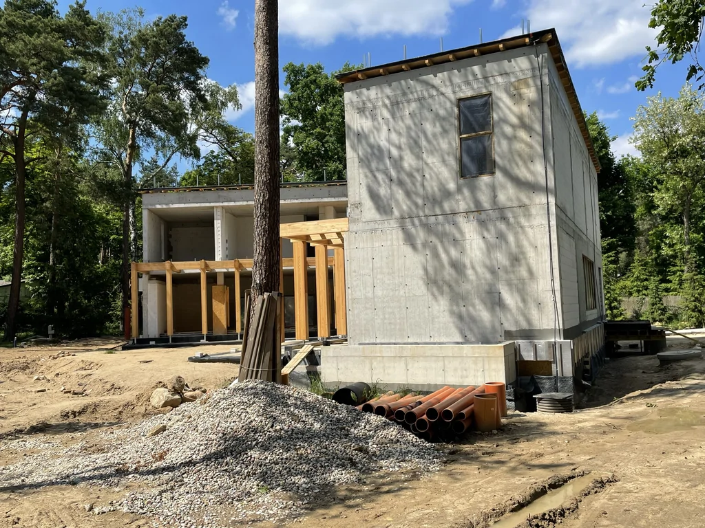 Boczny widok domu jednorodzinnego z wysoką ścianą żelbetową oraz instalacjami przygotowanymi przy elewacji