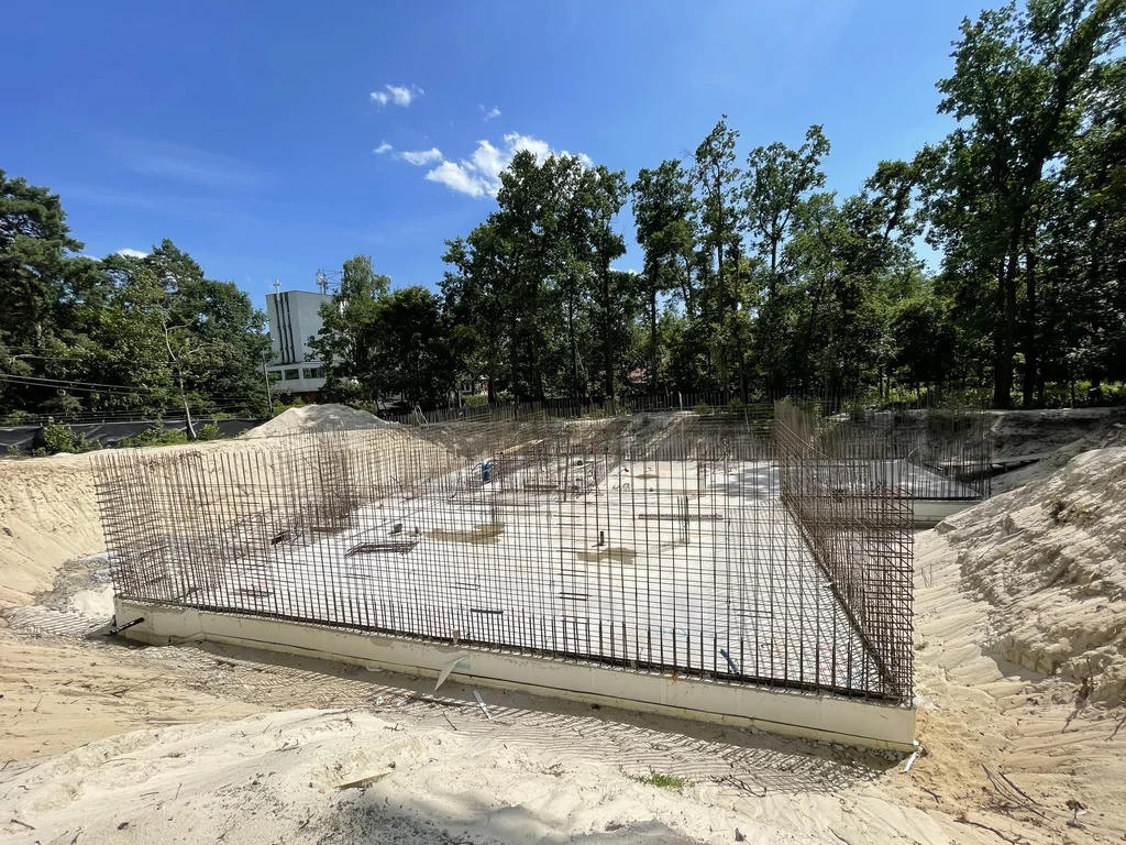 Szeroki widok wykopu z płytą fundamentową i przygotowanym zbrojeniem ścian żelbetowych