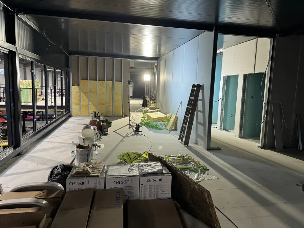 Przeszklona antresola toru gokartowego w trakcie wykończenia, z zabudową ścian, izolacją i materiałami budowlanymi.