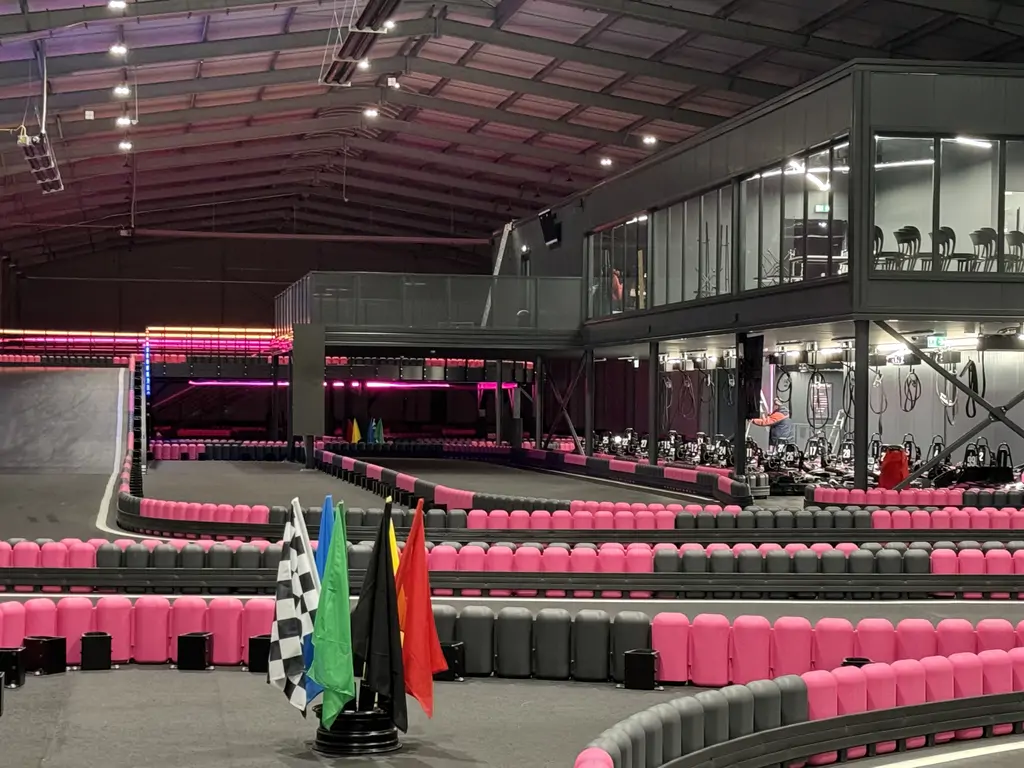 Gotowy tor gokartowy w hali, z neonowym oświetleniem, bandami w kolorze różowym i czarnym oraz strefą flag.