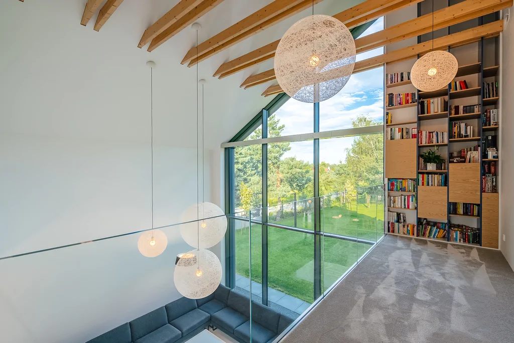 Antresola z wysoką biblioteczką i panoramicznym widokiem na ogród przez przeszklenie.