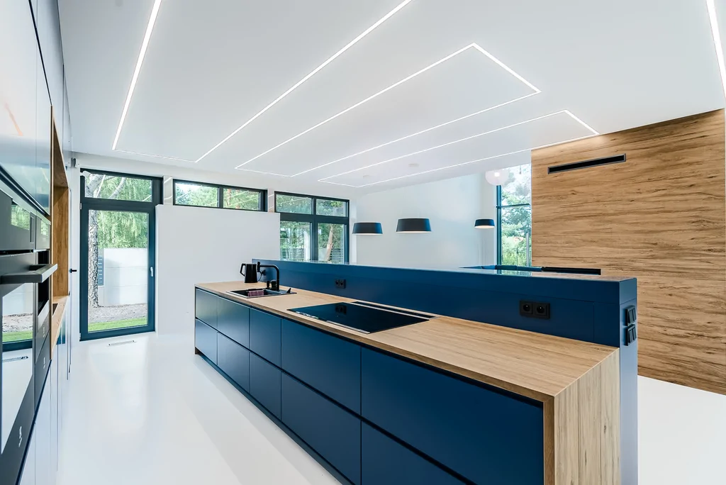 Długa wyspa kuchenna z drewnianym blatem i granatową zabudową w otwartej przestrzeni.