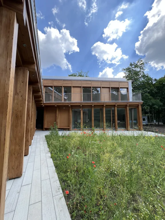 Widok z dziedzińca na nowoczesny dom z drewnianą elewacją, balkonem i dużymi przeszkleniami