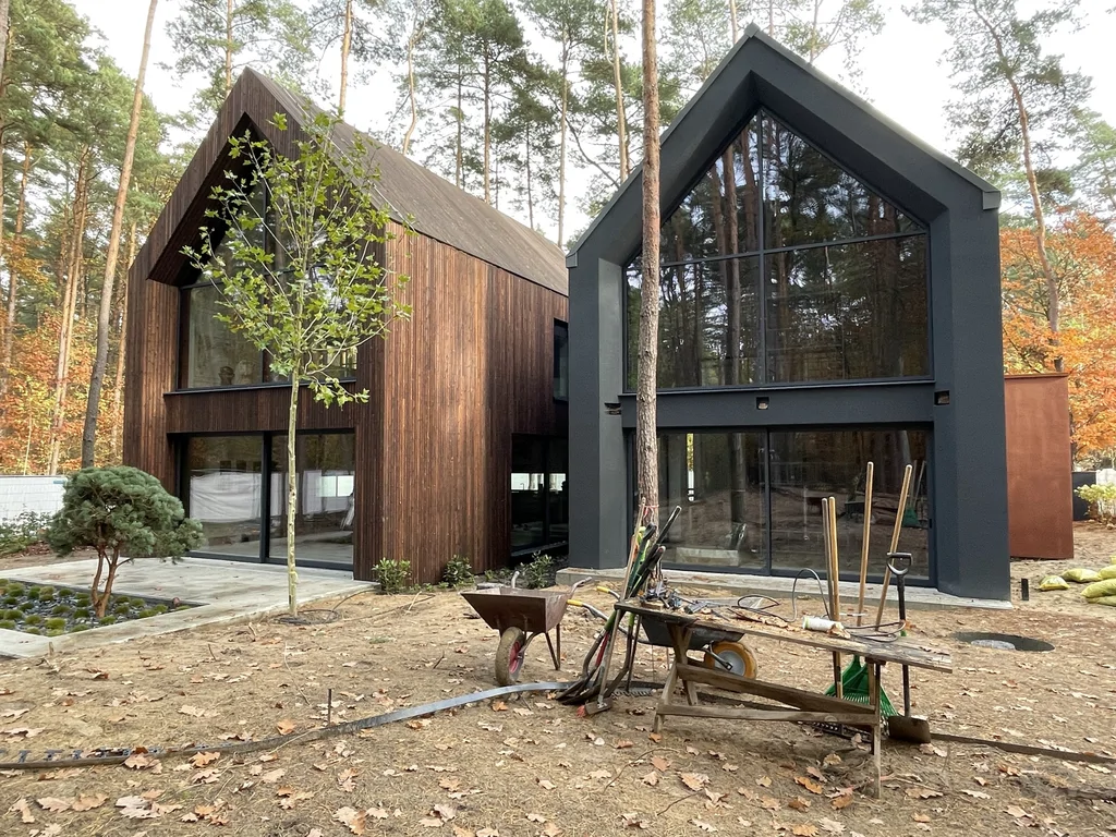 Widok dwóch nowoczesnych brył domu w Magdalence z dużymi przeszkleniami, drewnem i ciemną elewacją