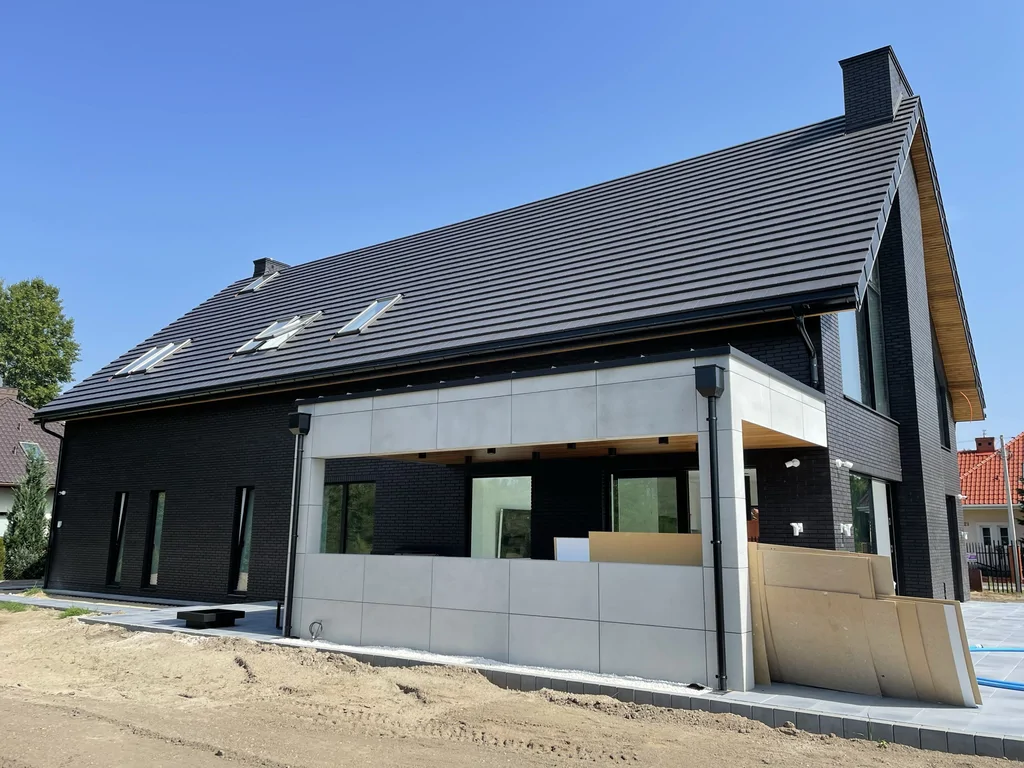 Boczna elewacja z zadaszonym tarasem – połączenie czarnej cegły i jasnych płyt