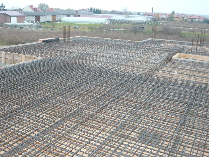 Zbrojenie stropu żelbetowego z wystającymi prętami pod słupy, widok na plac budowy
