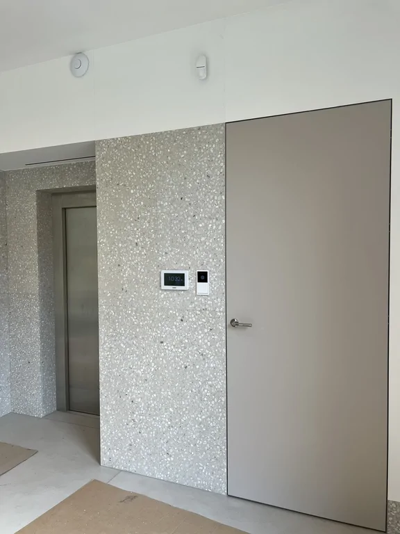 Strefa komunikacji z windą, ukrytymi drzwiami i ścianą wykończoną lastrykiem