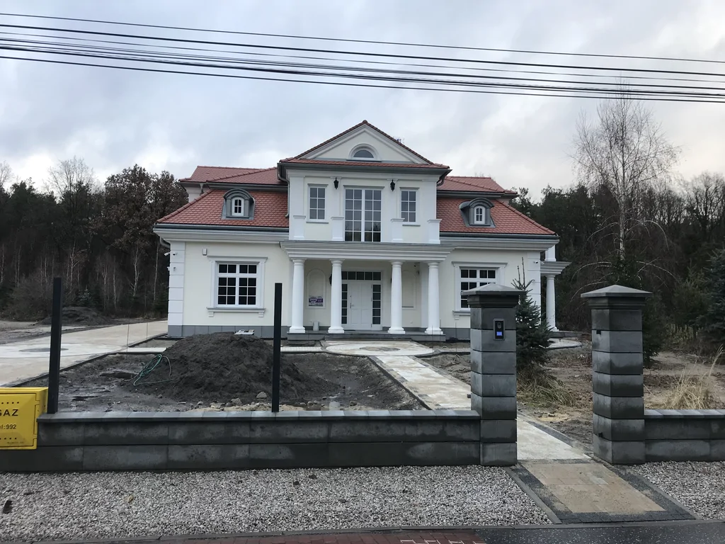 Budowa domu jednorodzinnego, styl dworkowy, dachówka z karpiówki, biała elewacja, bonie, lukarny, kominy, biała stolarka okienna, ogrodzenie 