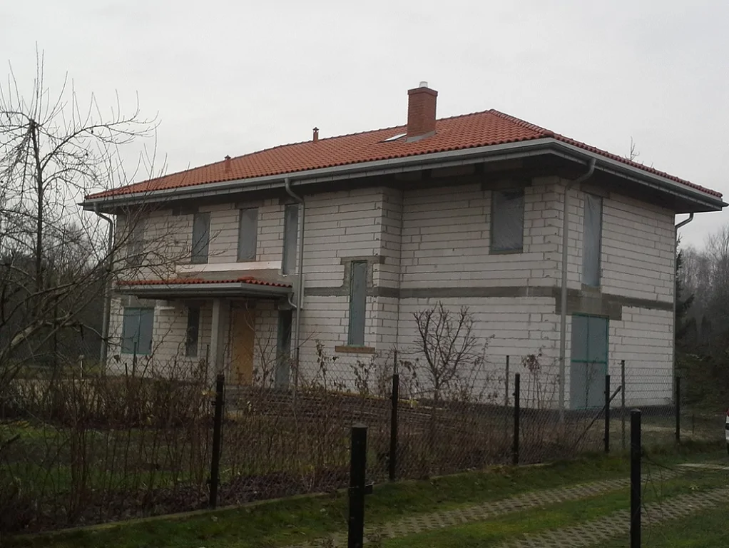 Budowa Domu jednorodzinnego widok z zewnątrz, wykonane mury oraz elementy konstrukcyjne; gotowy dach zaślepione otwory okienne