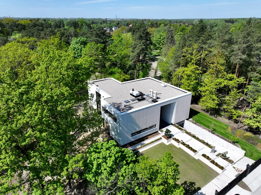 Widok z lotu ptaka na nowoczesny dom z frontowym placem wejściowym i działką otoczoną gęstą zielenią