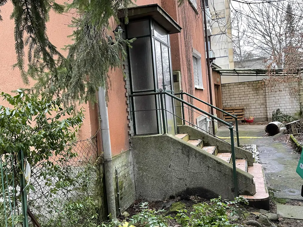 Stan istniejący przed remontem – boczna elewacja budynku z wejściem i schodami terenowymi.