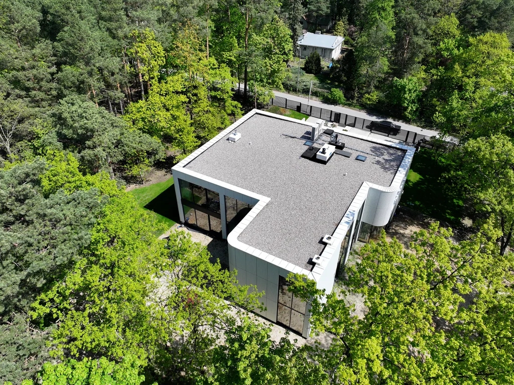 Ujęcie z lotu ptaka na dach nowoczesnego domu oraz tylne elewacje otoczone wysokimi drzewami