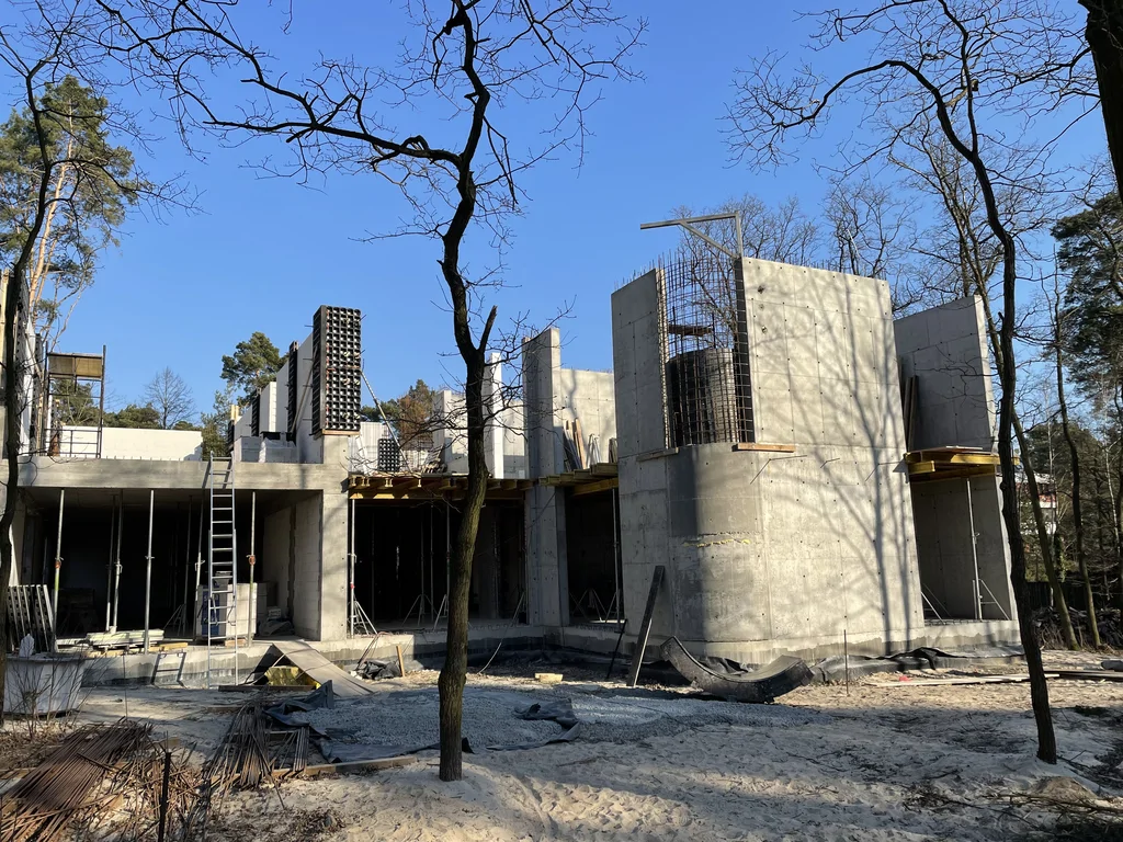 Stan surowy nowoczesnego domu w Konstancinie z żelbetową konstrukcją, zaokrąglonym narożnikiem i wysokimi ścianami