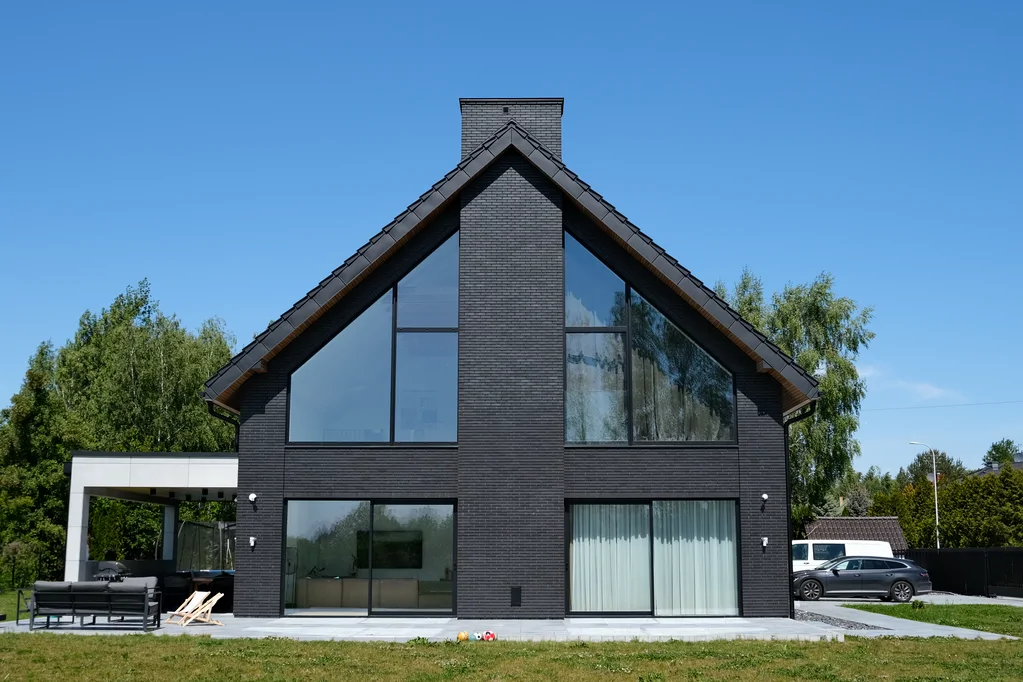 Elewacja szczytowa domu w Ruścu: centralny komin i przeszklenie dwukondygnacyjne od strony ogrodu.