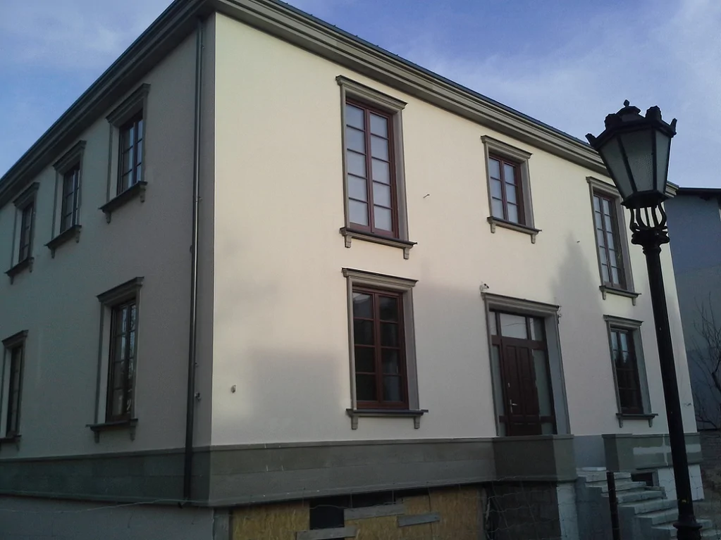 Widok na dom jednorodzinny, biała elwacja, ciemna stolarka okienna, schody wejściowe