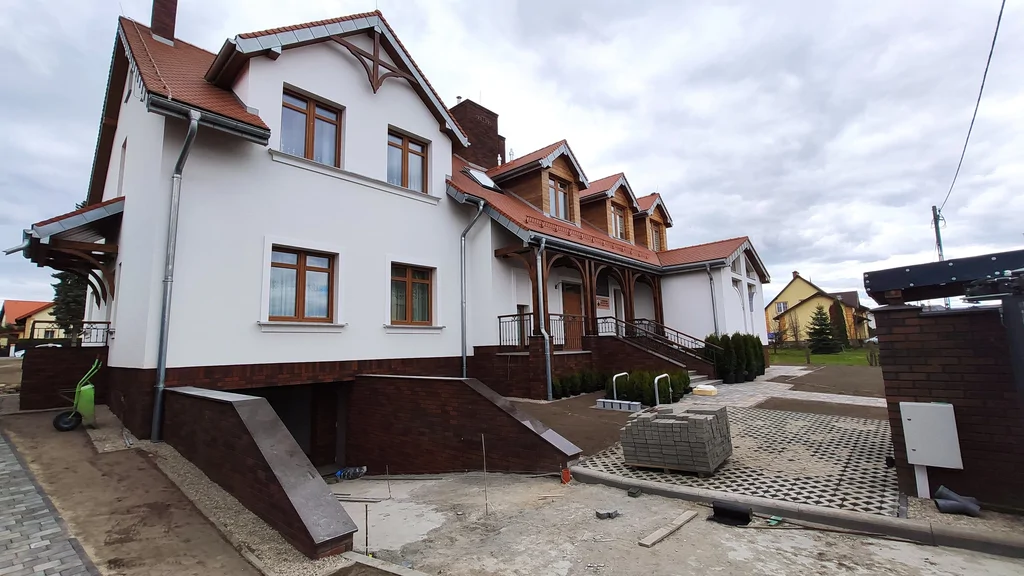 Boczna ścieżka przy domu zakonnym w Ostródzie, ze schodami i wysokimi oknami z łukami oraz witrażami