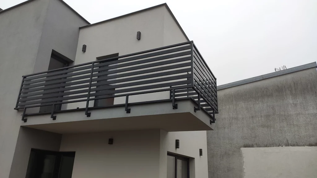 Budynek w stanie deweloperskim, dach płaski, jasna elewacja, barierki stalowe nad balkonem