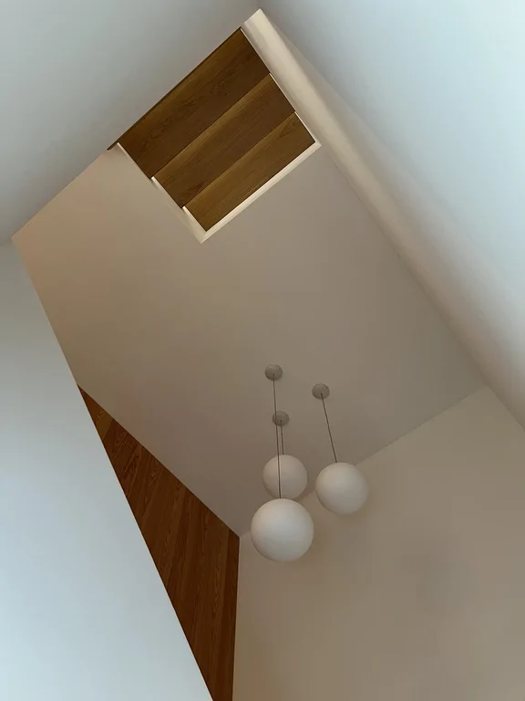 Wysoki sufit nad klatką schodową z trzema kulistymi lampami wiszącymi i drewnianymi detalami