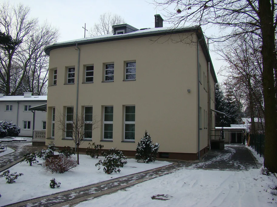 Widok narożnika i elewacji bocznej budynku po remoncie; wysokie przeszklenia i podjazd w zimie