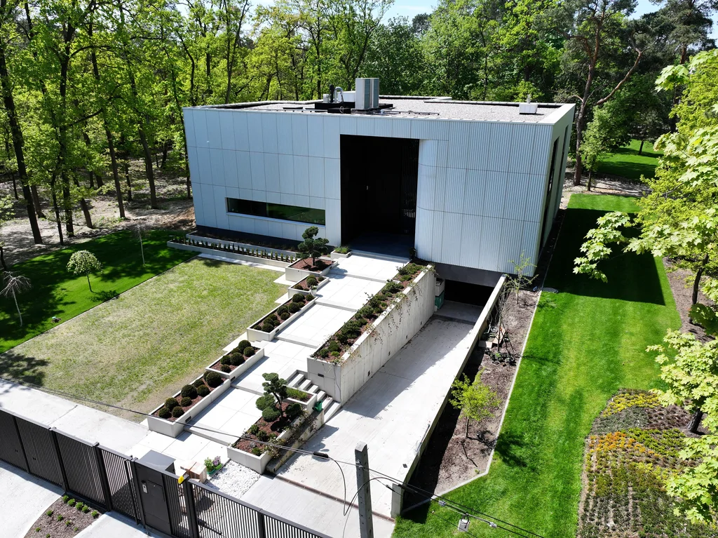 Frontowa elewacja domu z lotu ptaka z widocznym wejściem, zjazdem do garażu i uporządkowaną kompozycją zieleni