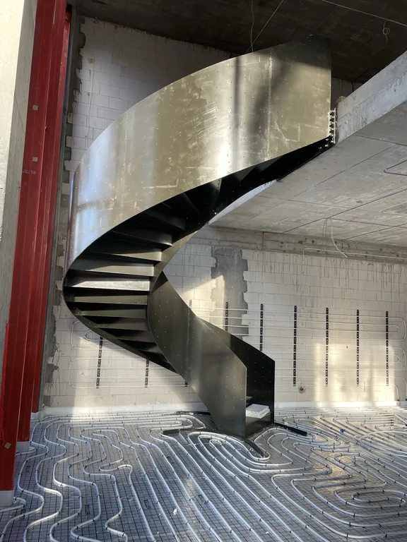 Nowoczesne stalowe schody kręcone we wnętrzu domu jednorodzinnego podczas prac wykończeniowych