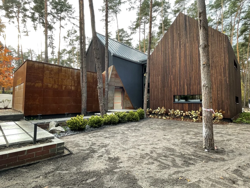 Front nowoczesnego domu w lesie z cortenem, drewnianą elewacją i geometryczną formą dwóch brył