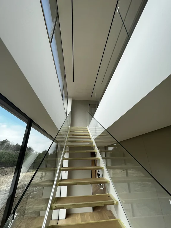 Widok w górę na schody ażurowe i wysoką przestrzeń z liniowymi szczelinami w suficie.