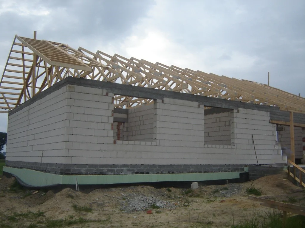 Narożnik domu w stanie surowym z zamontowanymi wiązarami dachowymi