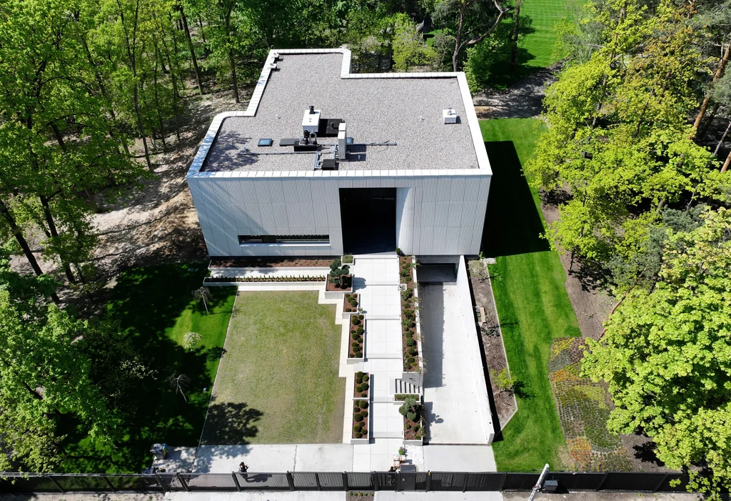 Widok z góry na nowoczesny dom z płaskim dachem, cofniętym wejściem i uporządkowaną kompozycją ogrodu frontowego