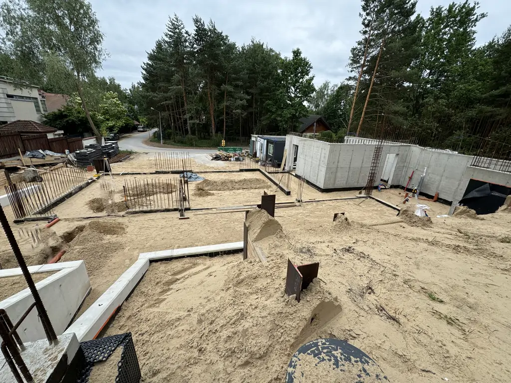 Szeroki widok na plac budowy z wykonanymi ścianami piwnicy, fundamentami i przygotowaniem pod dalszą konstrukcję.