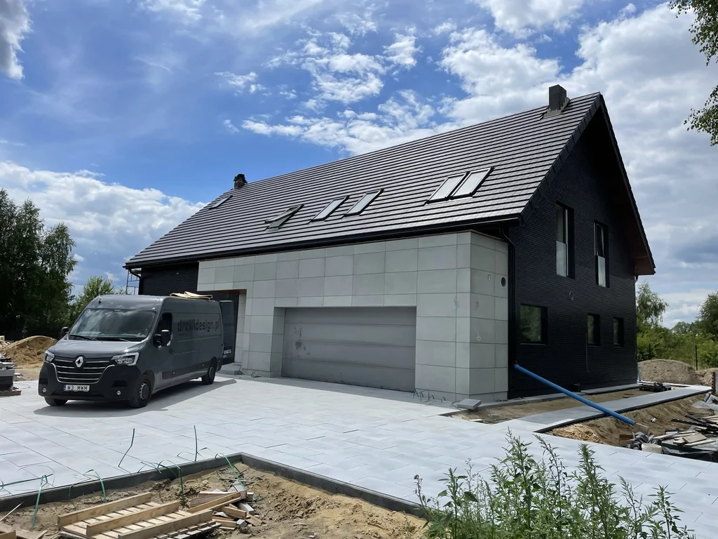 Strefa wjazdu i garaż – okładzina z jasnych płyt, czarna bryła domu