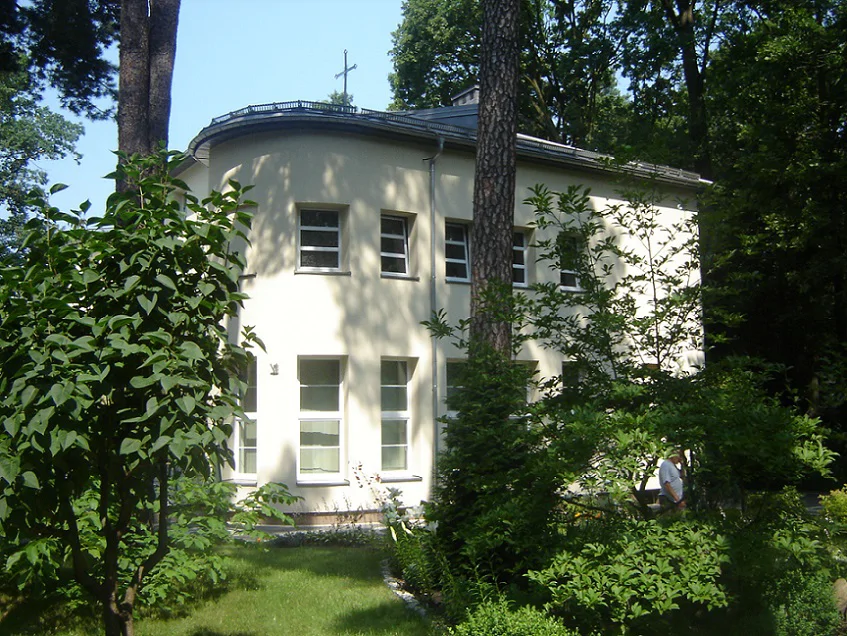 Budynek po remoncie w otoczeniu zieleni; widok elewacji z wysokimi oknami latem.