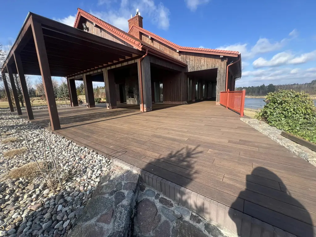 Ogólny widok wyremontowanego tarasu z zadaszoną strefą wypoczynkową, kamiennym grillem i elewacją z drewna.