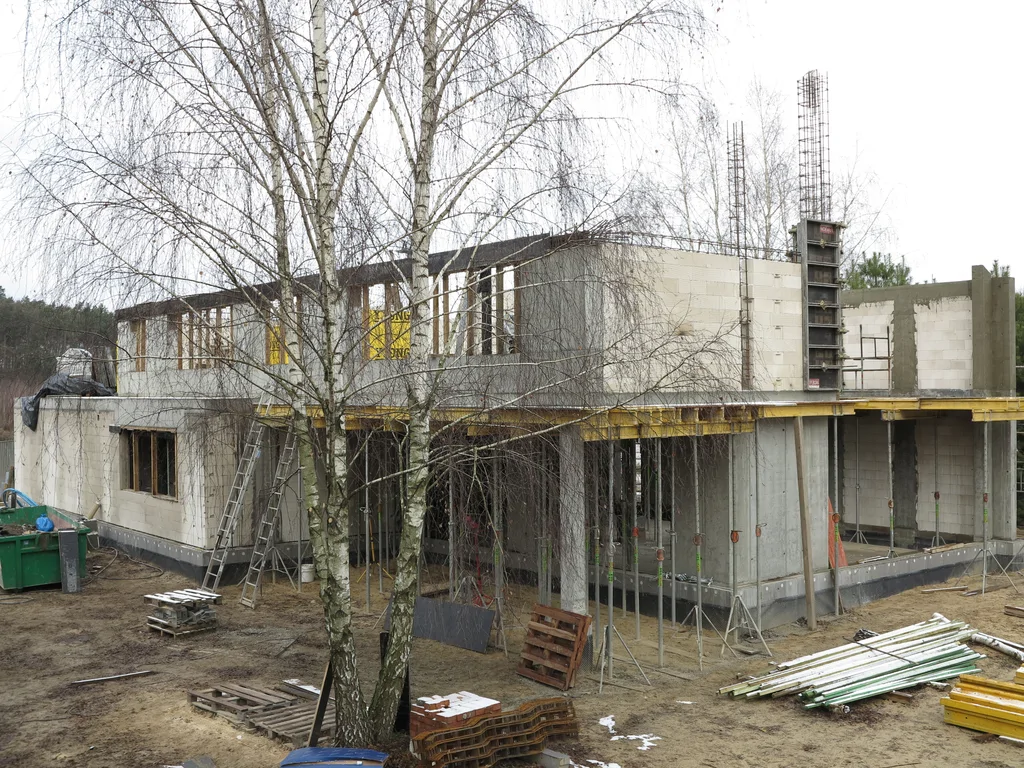 Budowa domu w stanie surowym, ściany z silikatów elementy żelbetowe, stemple podpierające nawis 