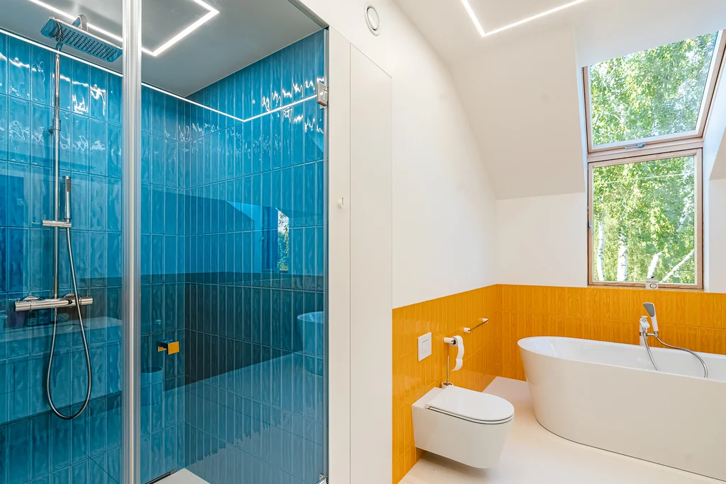 Łazienka z niebieską kabiną prysznicową, wolnostojącą wanną i pomarańczowymi płytkami ściennymi.