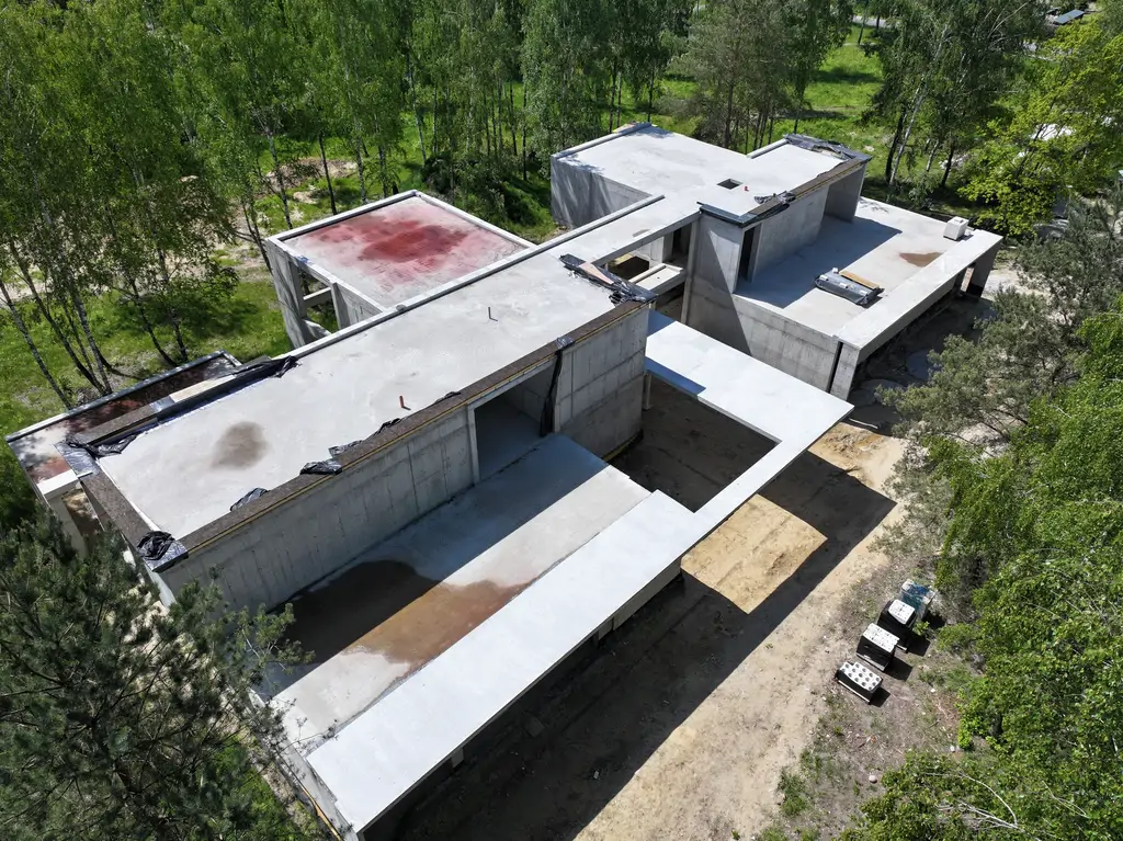 Widok z drona na żelbetową konstrukcję nowoczesnej willi z płaskimi dachami i rozbudowanymi podcieniami.