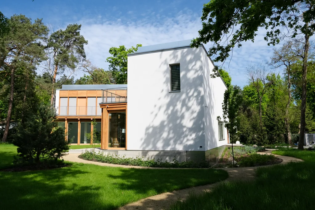 Widok na boczną elewację domu i ogród z wijącą się ścieżką oraz wysoką białą ścianą budynku