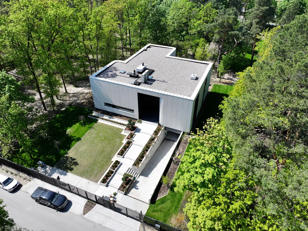 Szerokie ujęcie z drona przedstawiające front budynku, ogrodzenie posesji i leśne otoczenie działki