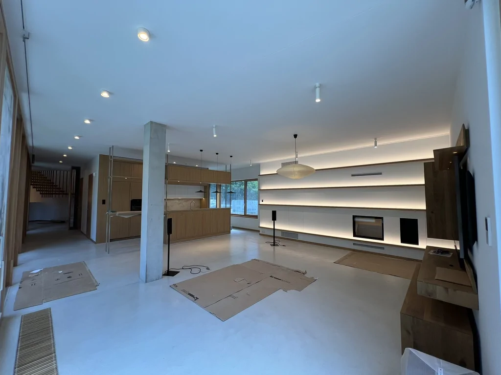 Przestronny salon z kuchnią, podświetlaną zabudową ścienną i minimalistycznym wykończeniem