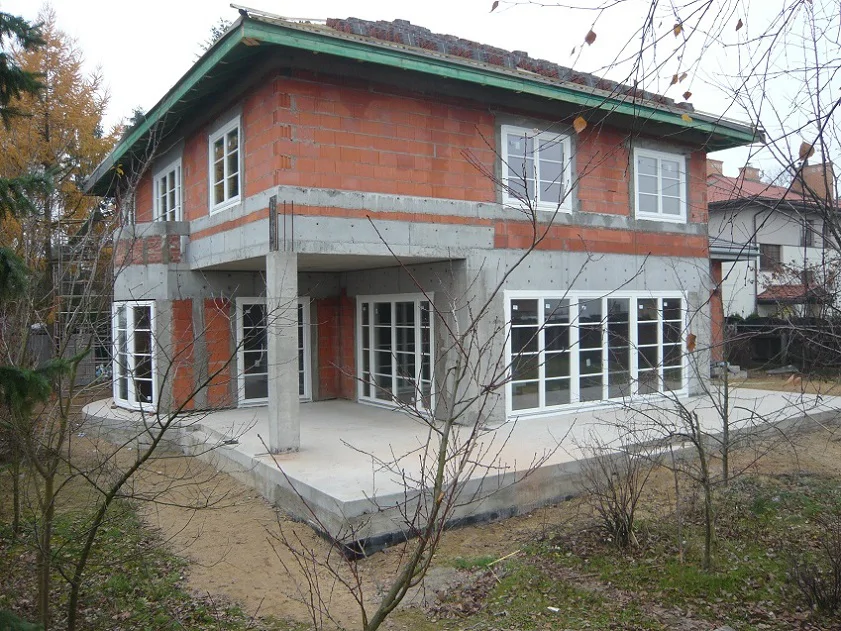 widok narożny domu z tarasem i dużymi oknami, nieukończony teren wokół