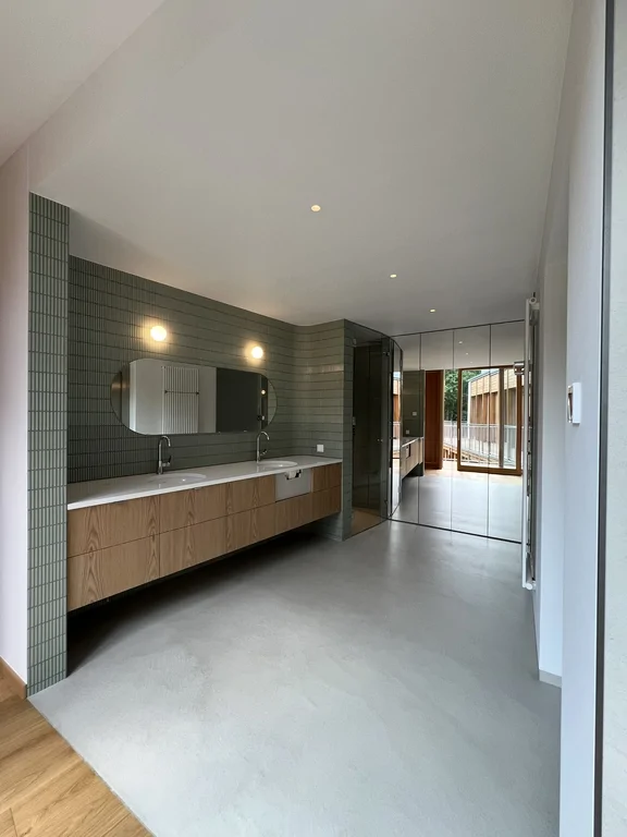 Łazienka z przeszklonym prysznicem, lustrzaną zabudową i zieloną okładziną ścienną