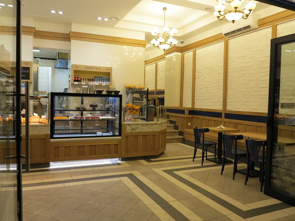 zdjęcie piekarni wewnątrz, kasa, półki z pieczywem, w tle widach kilku stopniowe schodki, na ścianach kamień i drewno 