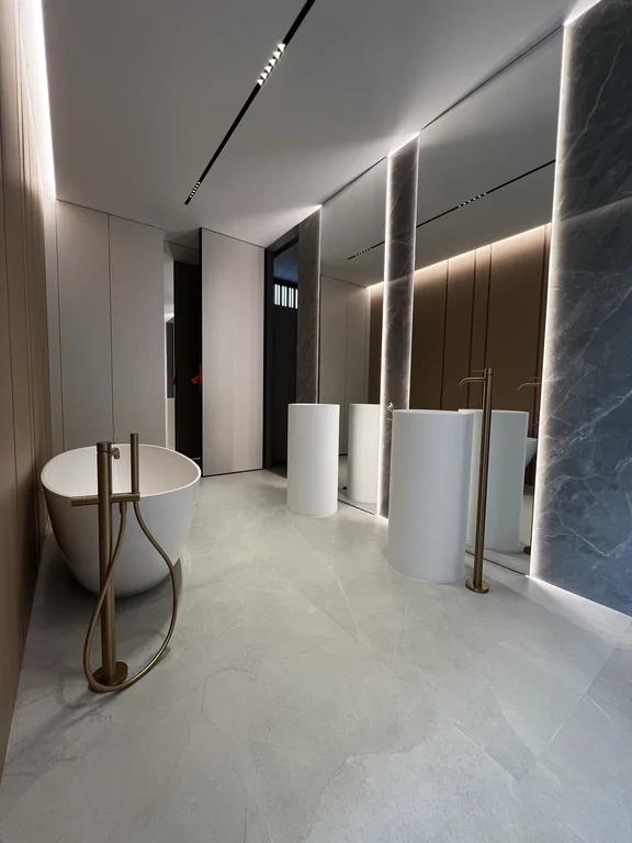 Przestronna łazienka z wolnostojącą wanną, umywalkami na postumentach i podświetlanymi pionami z kamienia/spieku.